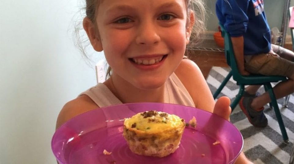 Child smiling, holding a purple plate with a small quiche.
