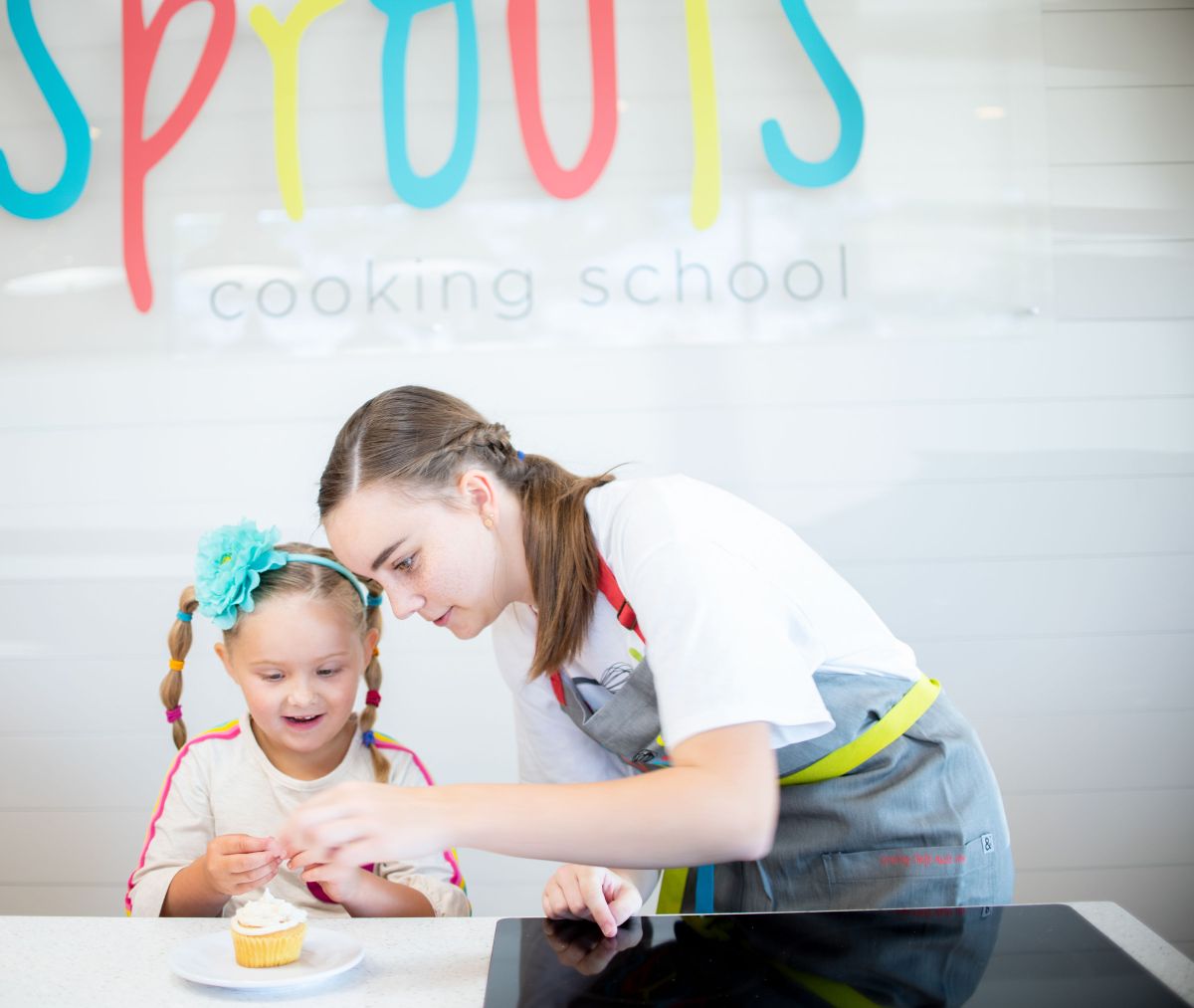Adult helping child decorate a cupcake in a cooking class setting.