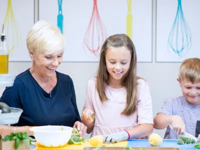 Smiling woman and two kids chopping vegetables in a bright kitchen.