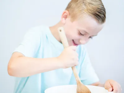 Smiling child mixing ingredients in a white bowl with a wooden spoon.
