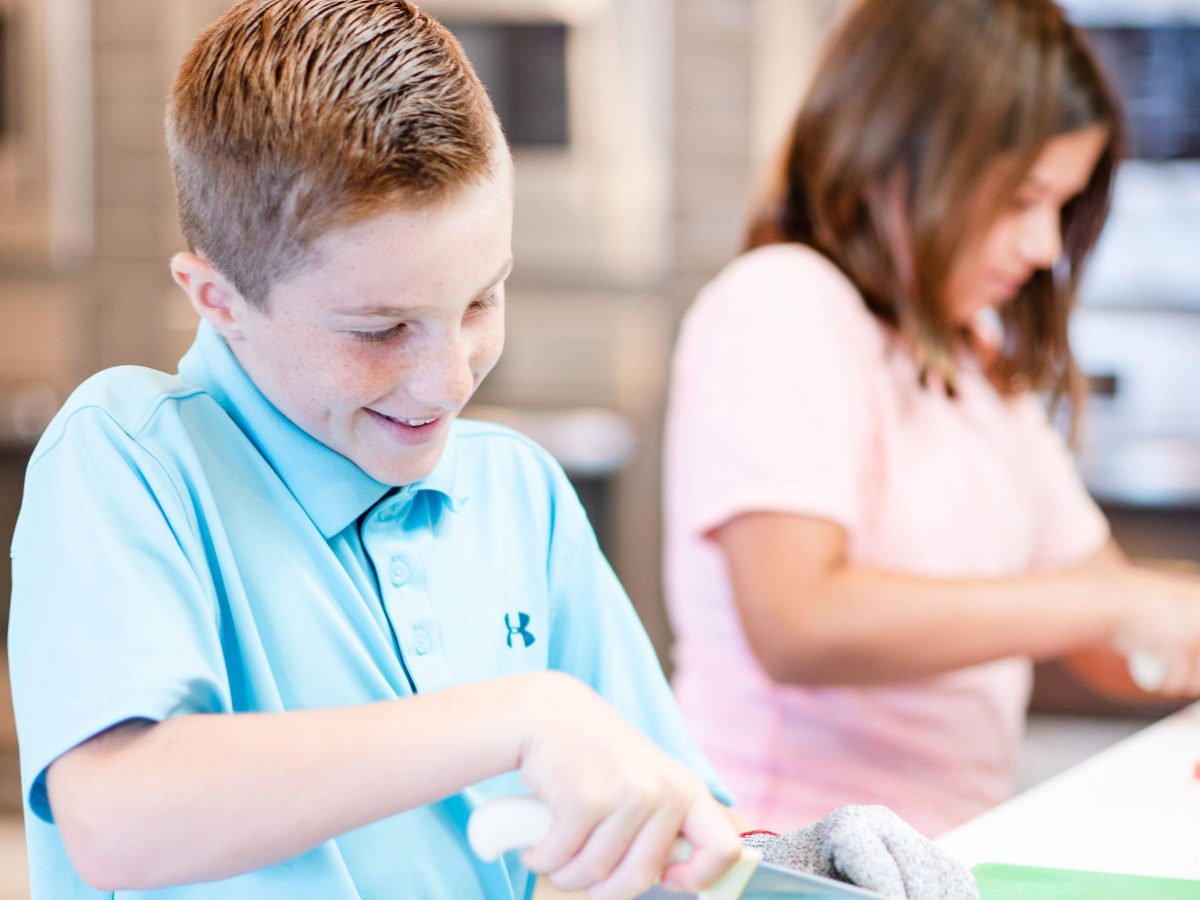 Two children in a kitchen, one chopping bell peppers on a green cutting board.