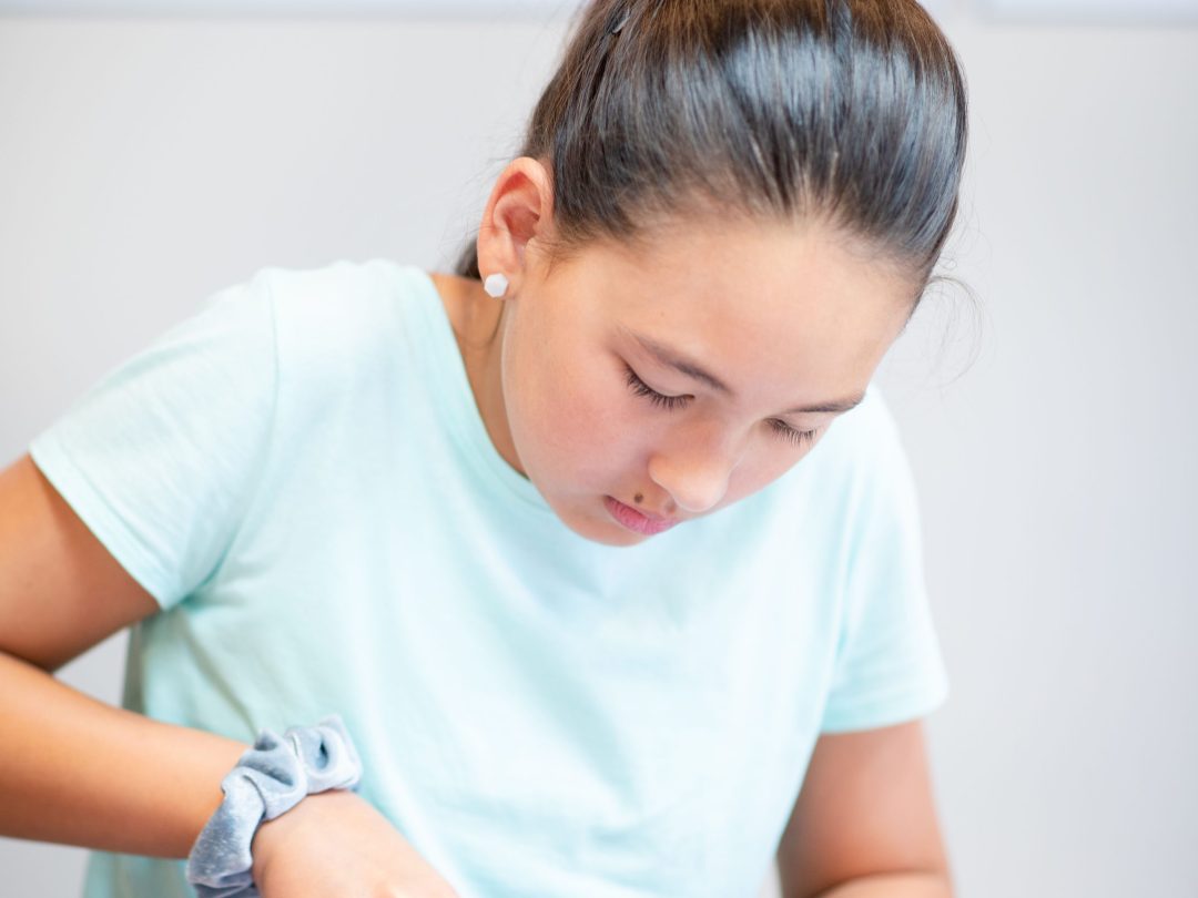 Girl wearing a glove cutting yellow pepper slices on a blue cutting board.