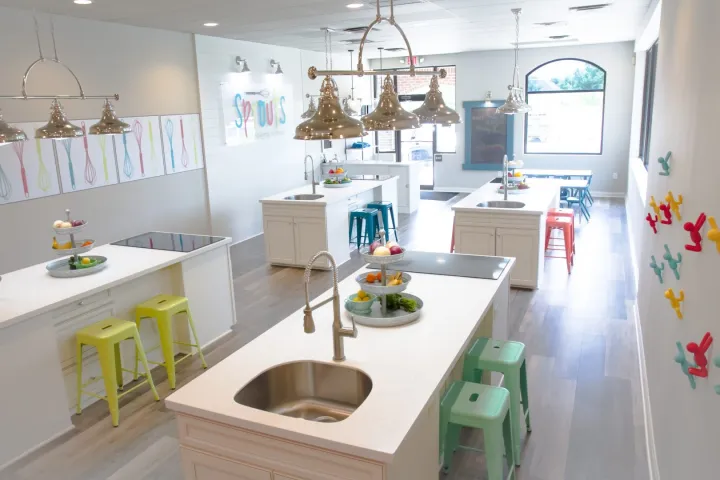 Bright kitchen space with multiple islands, colorful stools, and hanging pendant lights.