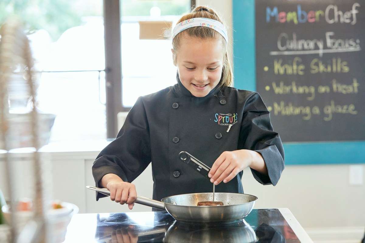 Young chef in black coat cooking with thermometer in kitchen.