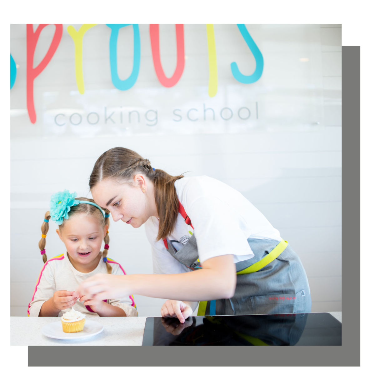 Two children decorating a cupcake at a cooking school counter.