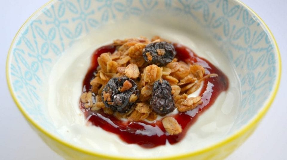 Bowl of yogurt with granola, raisins, and red jam on top.