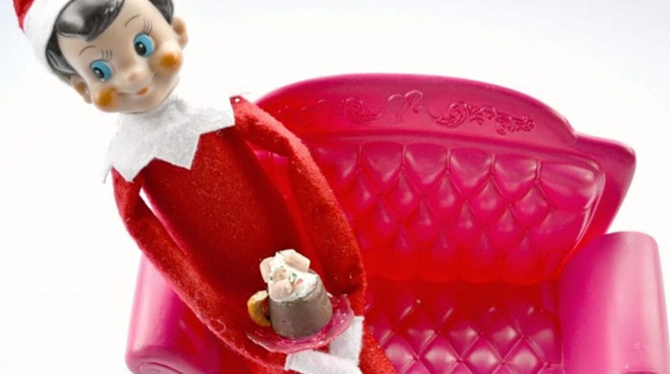 Elf doll holding dessert stands on a pink plastic sofa.