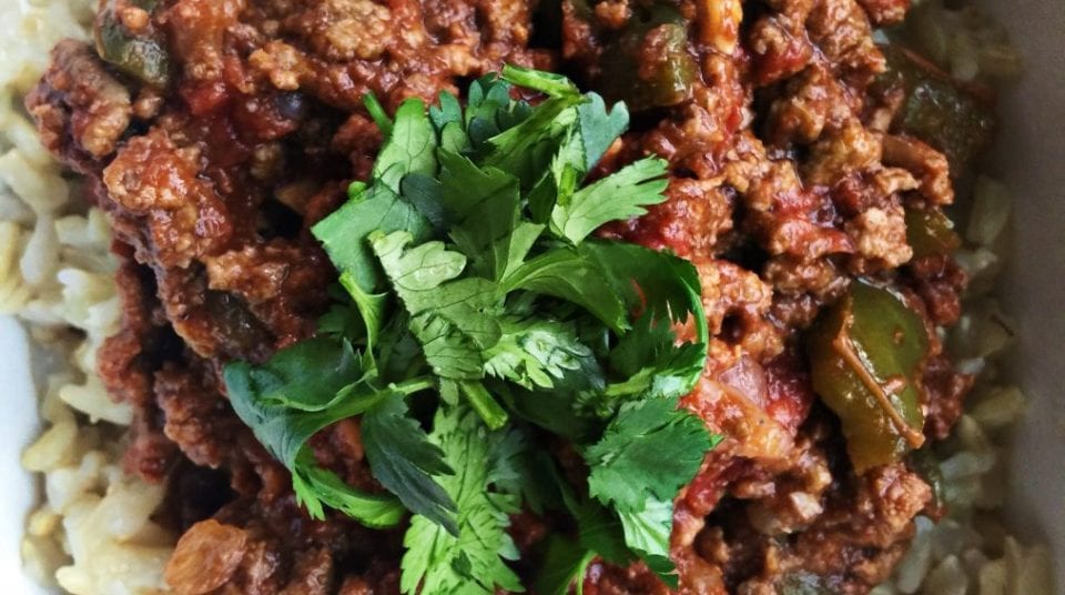 Close-up of a meat stew with green pepper and cilantro garnish on rice.