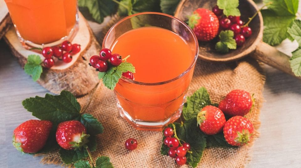 Glass of orange juice with strawberries and red currants on burlap.