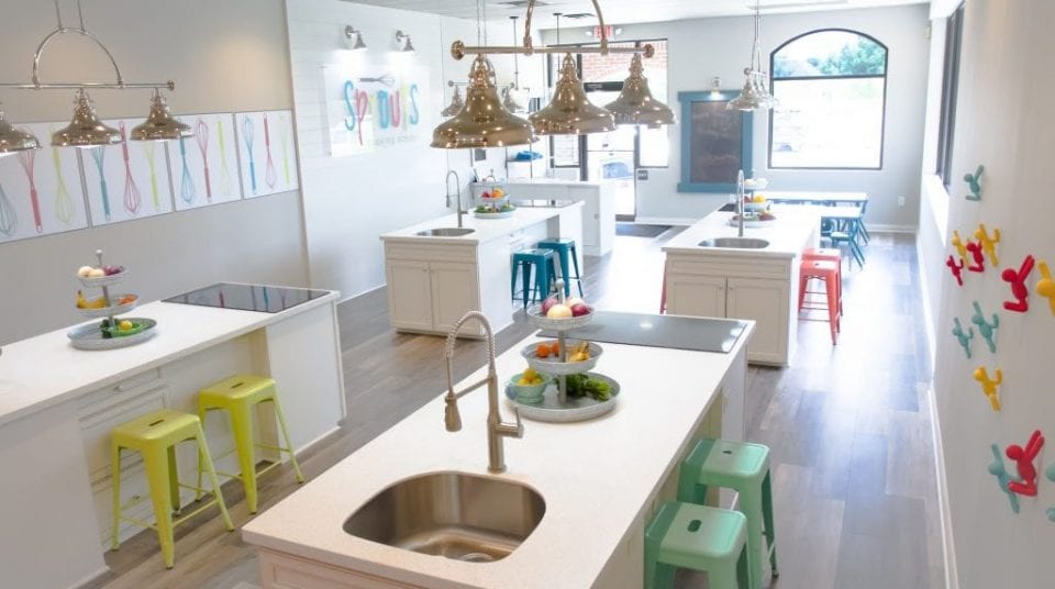 Bright kitchen classroom with islands, colorful stools, overhead lights, and wall decor.