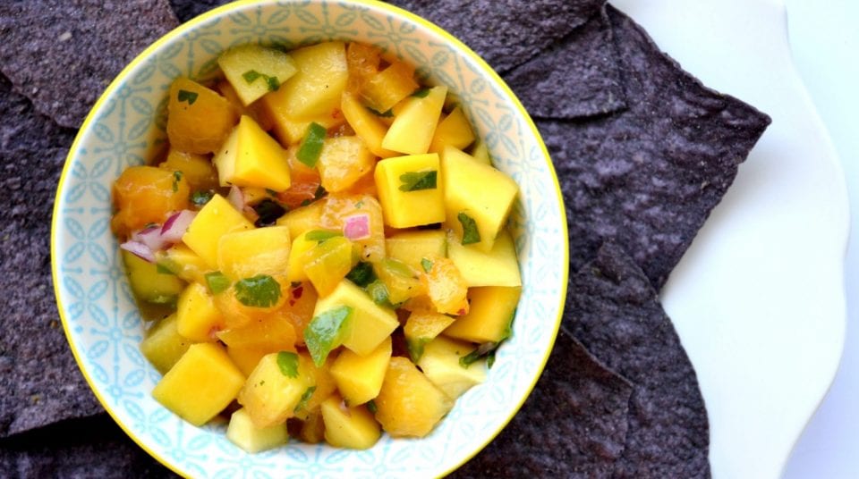 Bowl of mango salsa with blue tortilla chips on a white plate.