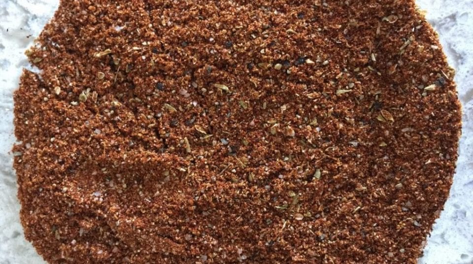 Close-up of a pile of red spice mix with herbs on a light surface.