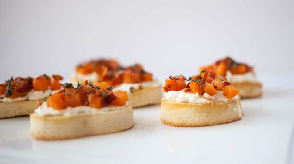 Close-up of bruschetta topped with diced pumpkin on a white surface.