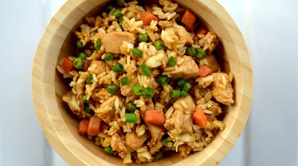 Bowl of fried rice with chicken, peas, and carrots on a white background.