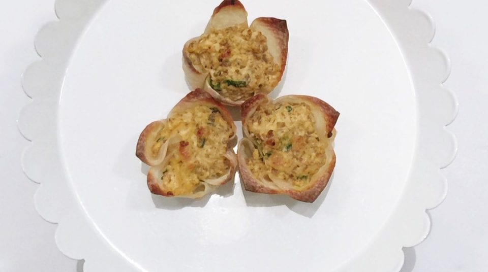 Three baked wonton cups filled with a creamy mixture on a scalloped white plate.
