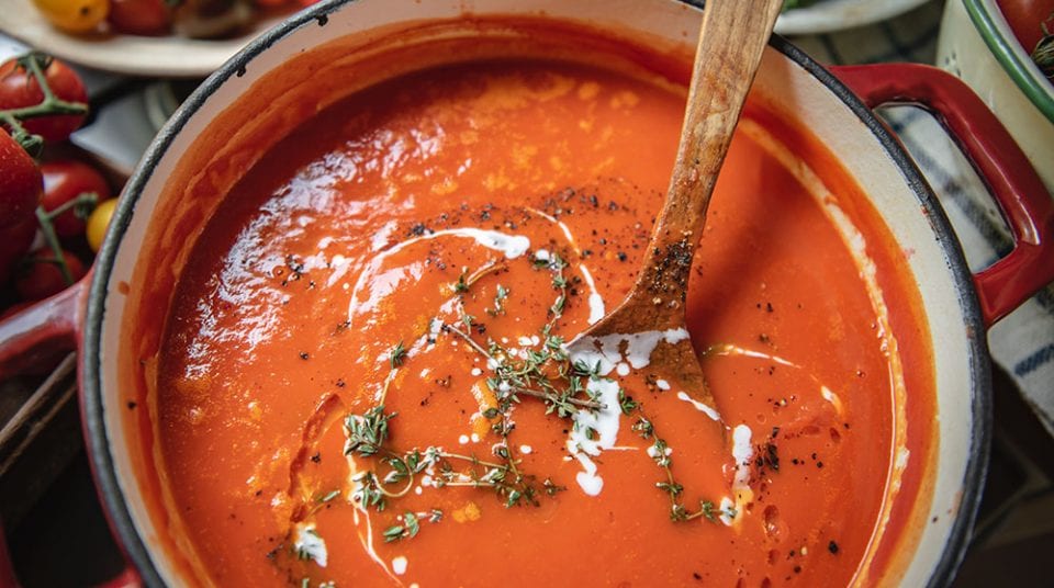 Tomato soup in a pot with wooden spoon, garnished with cream and thyme.