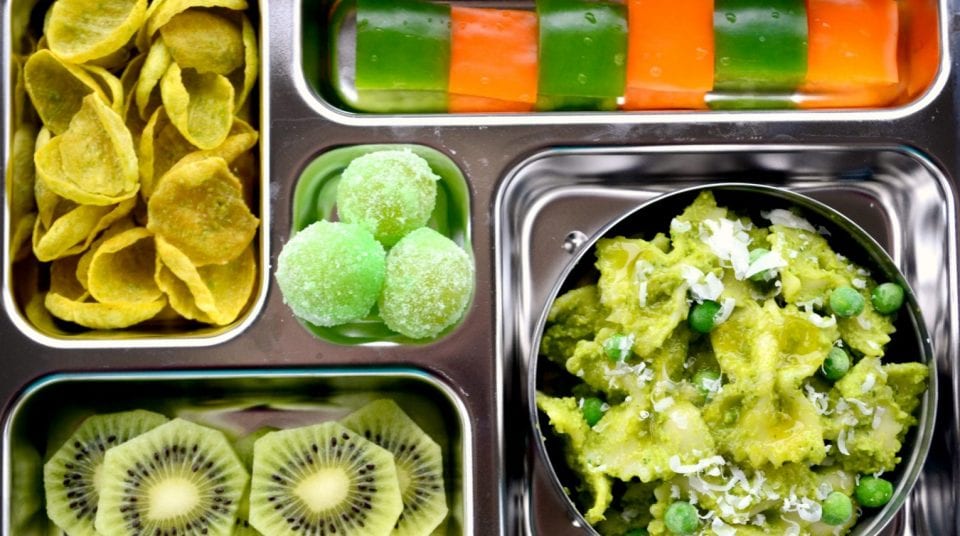 Bento box with pasta, peas, kiwi, chips, gummy balls, and layered jelly.