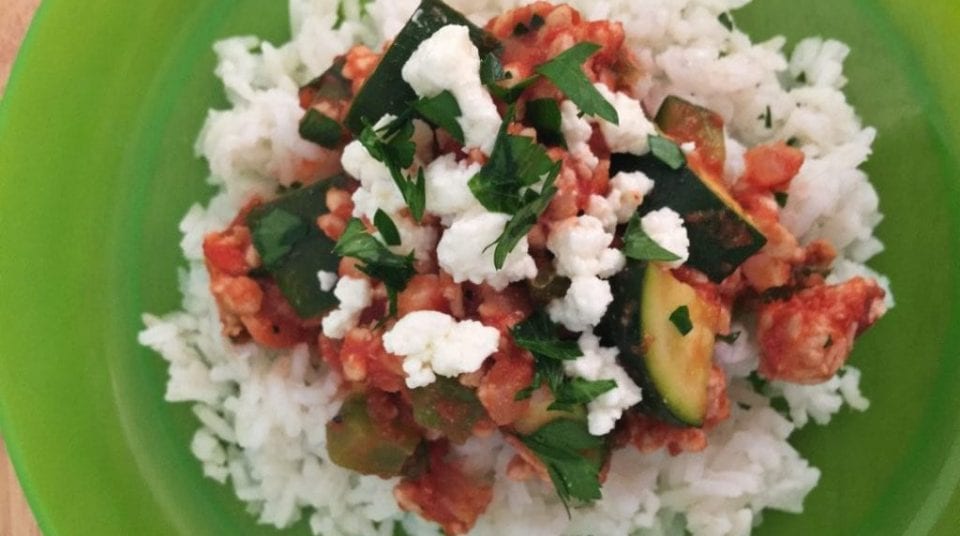 Rice topped with vegetables, sauce, and crumbled cheese on a green plate.