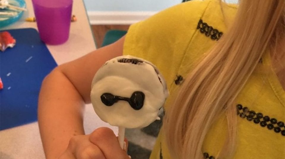 Girl holding a stick with a white candy featuring black sunglasses.