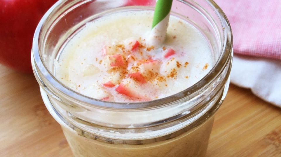 Mason jar with apple smoothie, red apple chunks, and sprinkled cinnamon.