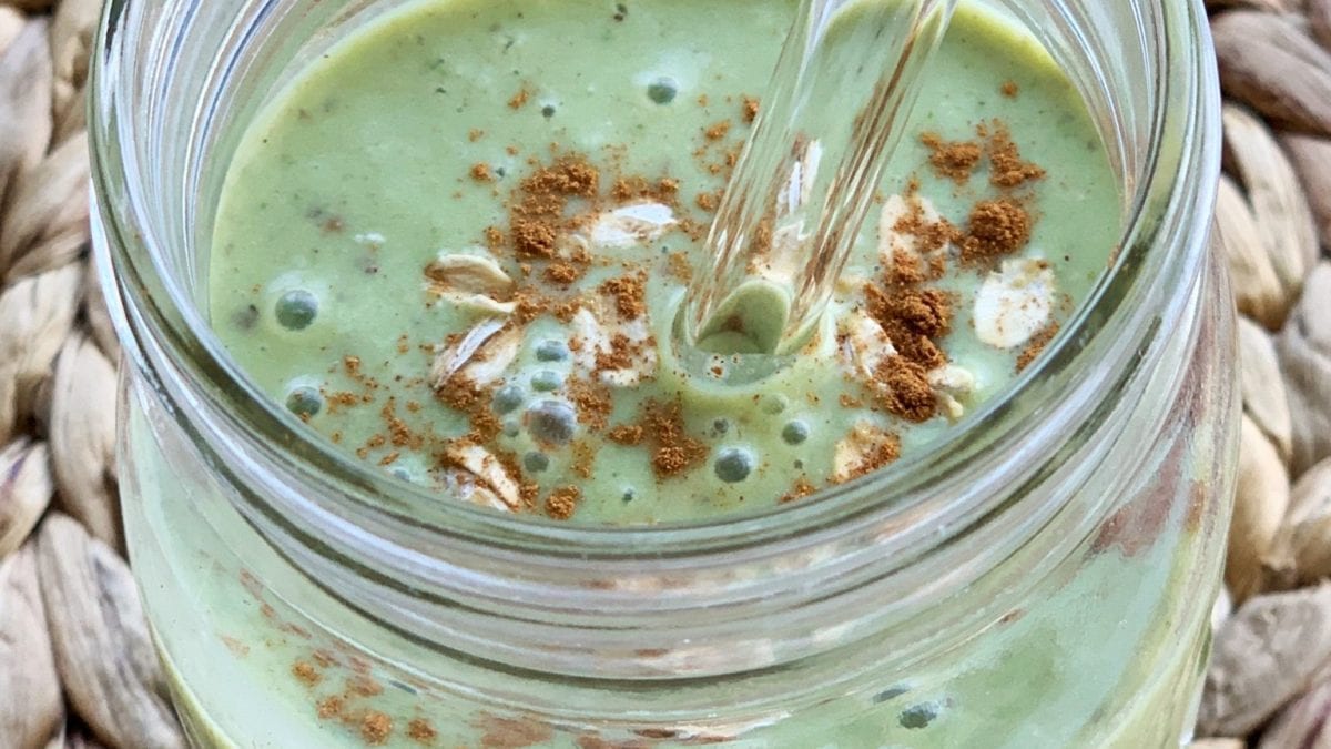 Green smoothie with oats and cinnamon in glass jar with straw.