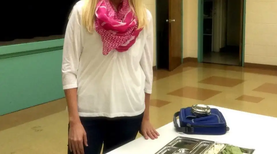 Person in white shirt and pink scarf standing by a table with containers.