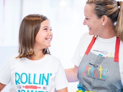 Smiling woman and girl cooking together at a kitchen counter.