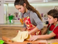 Two children in aprons roll out dough with a rolling pin in a kitchen.